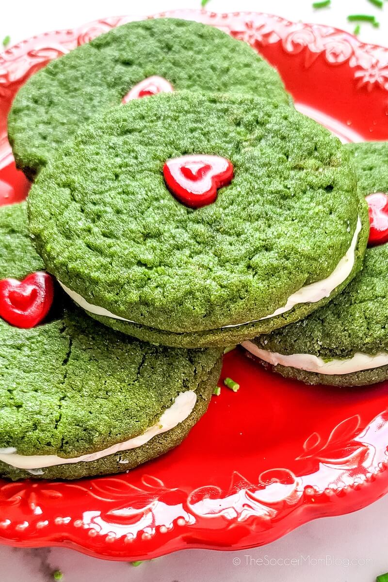 A plate of Grinch inspired green Cookie Sandwiches with a heart on top