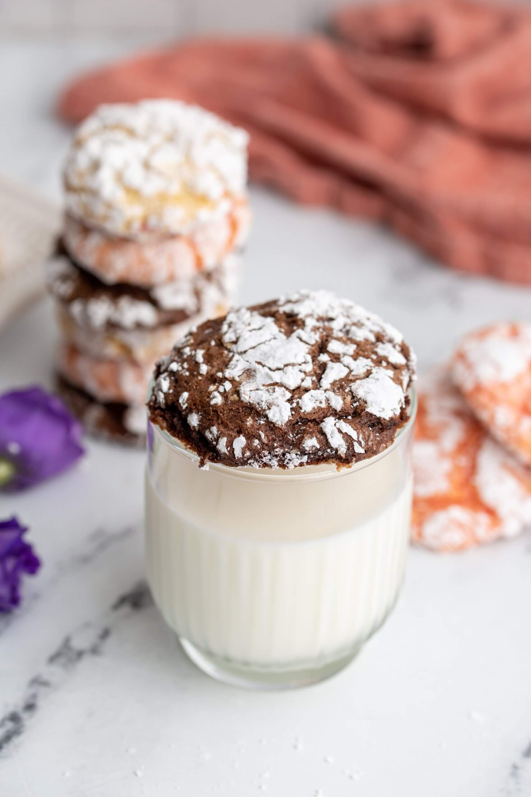 chocolate crinkle cookie on top of a glass of milk, stack of cookies in background