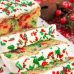 An iced Christmas loaf cake sliced to reveal red and green sprinkles inside