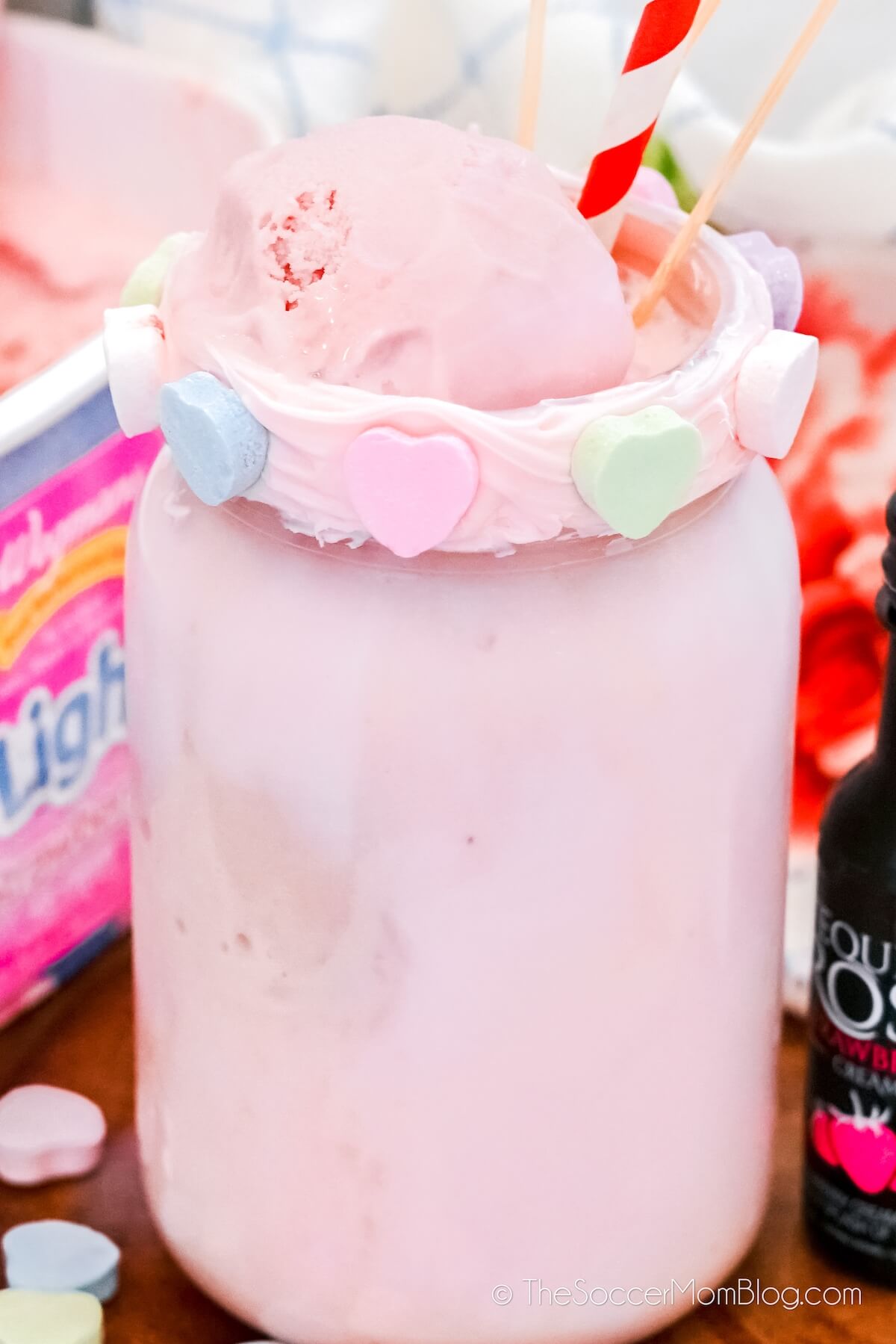 close up of a pink strawberry milkshake in mason jar with conversation heart rim