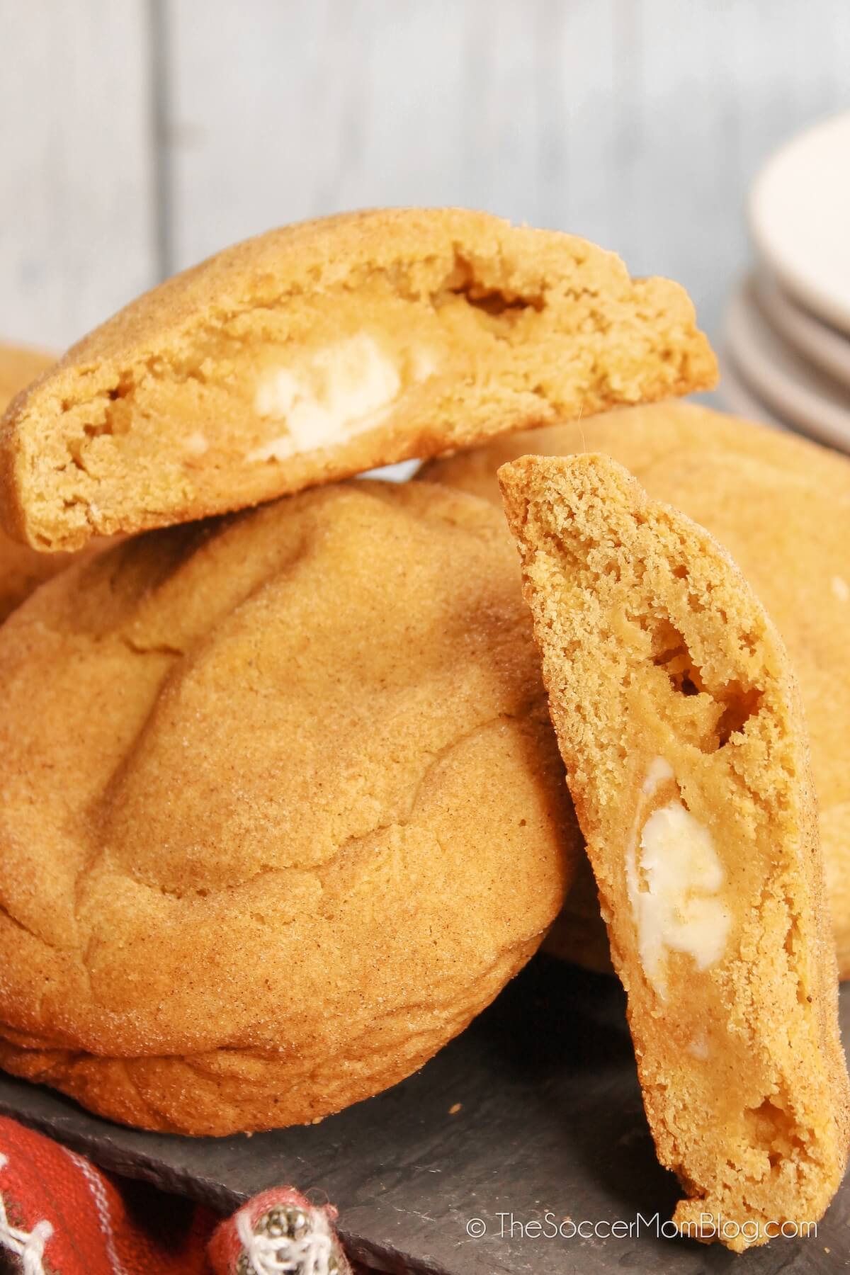 Pumpkin Cookies with one cut in half to show cheesecake filling, piled o serving plate