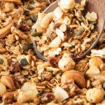 close up of homemade granola on baking sheet with wooden spoon