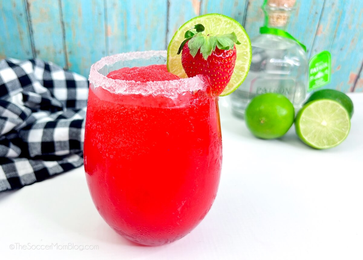 a frozen strawberry margarita with bottle of tequila in background