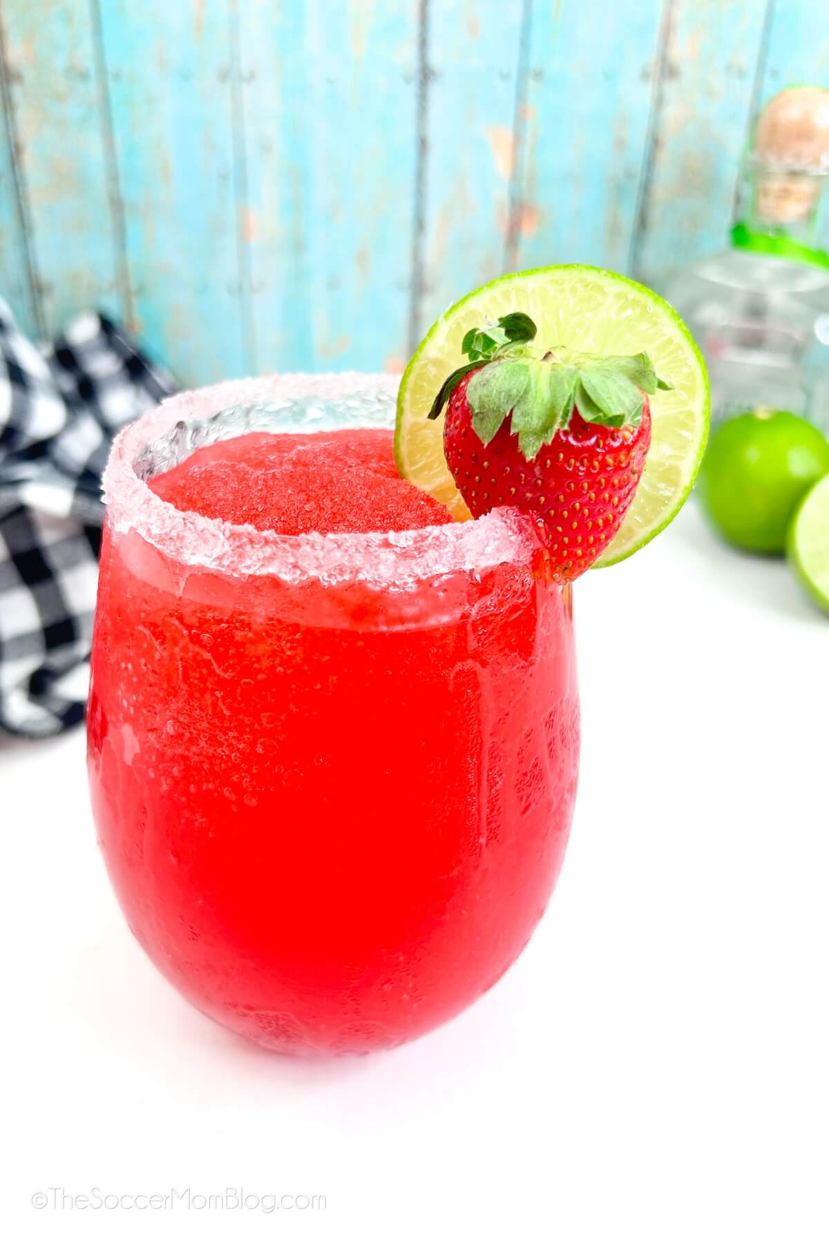 a glass with frozen strawberry margarita and a bottle of tequila in the background