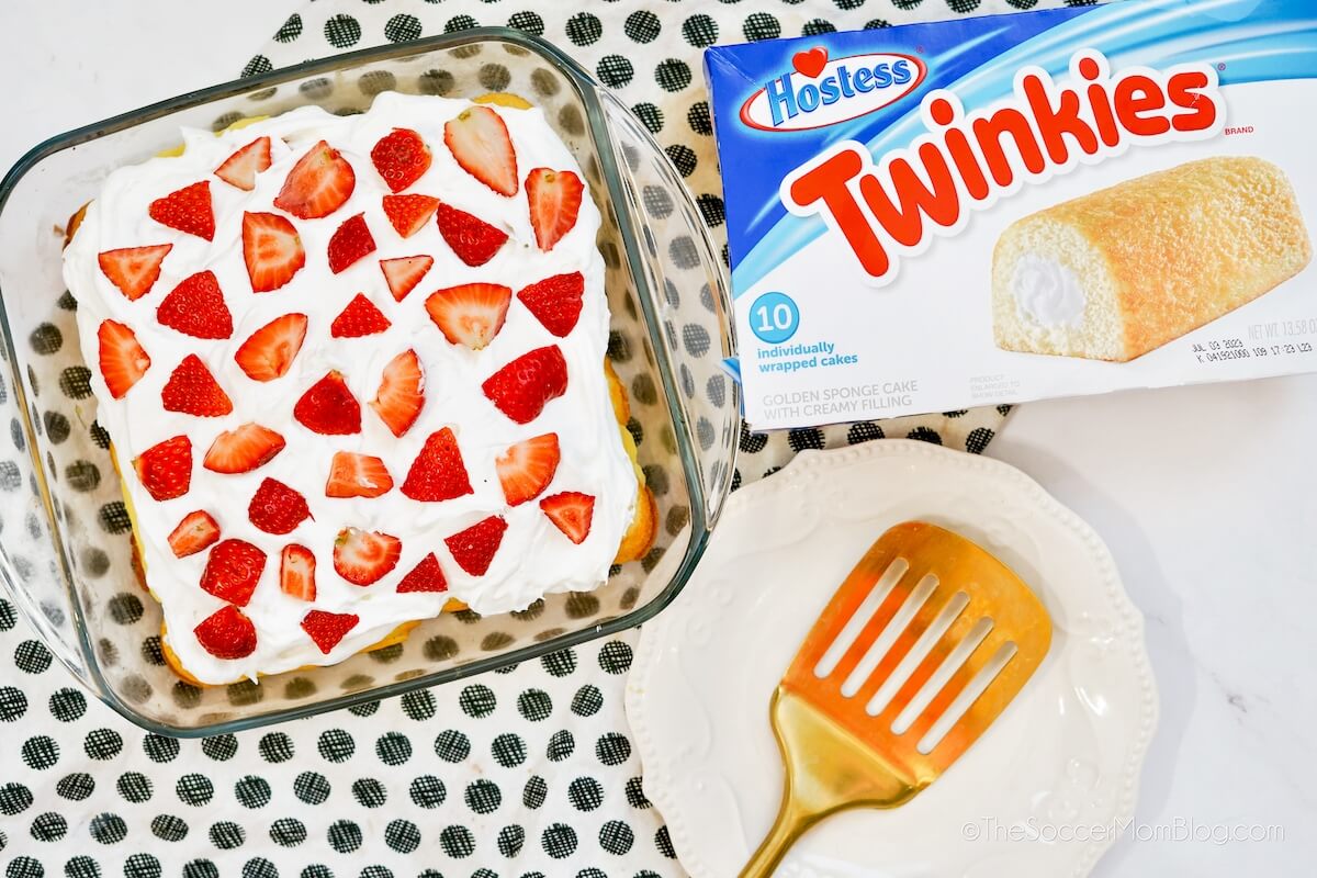 top down view of a no bake cake topped with Cool Whip and strawberries and a box of Twinkies