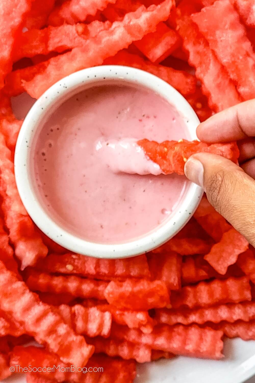 dipping a crinkle cut watermelon stick in pink fruit dip