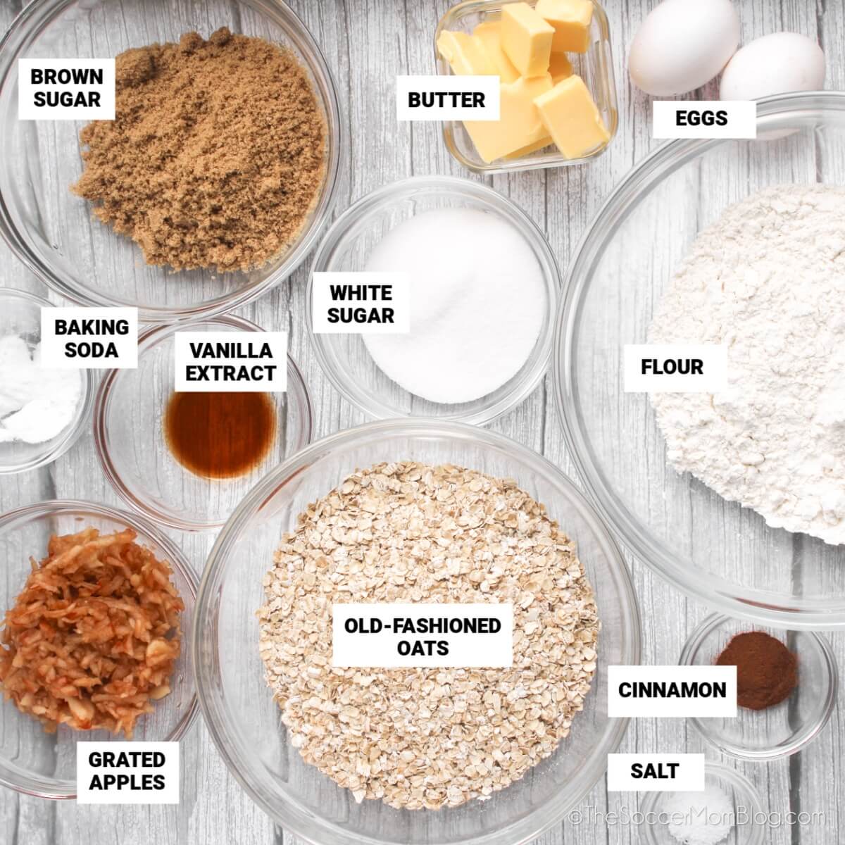 apple oatmeal cookie ingredients, with text labels: brown sugar, butter, eggs, flour, white sugar, vanilla extract, baking soda, grated apples, old-fashioned oats, cinnamon, salt