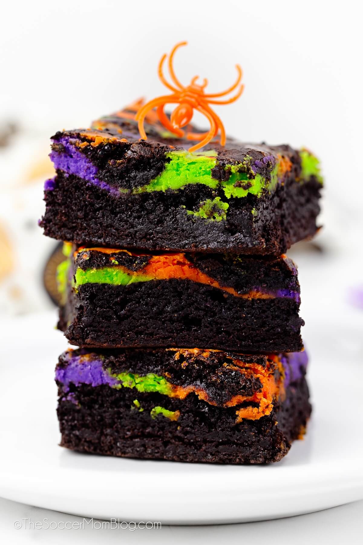 stack of 3 Halloween cheesecake brownies with orange, green, and purple swirls.