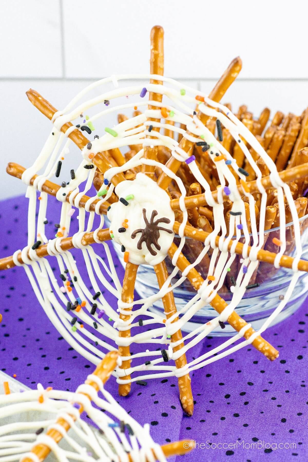 a pretzel spiderweb treat propped up on a jar of pretzels