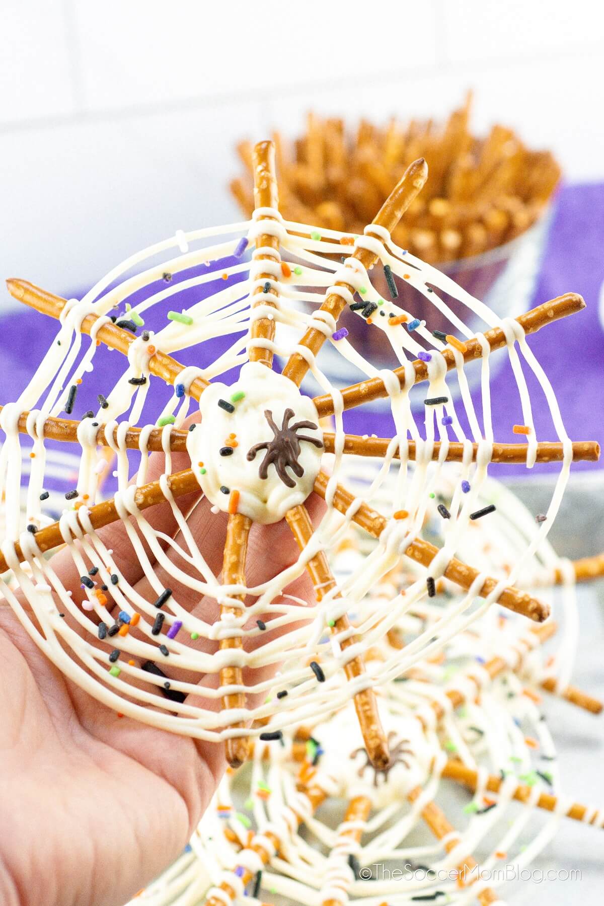 hand holding a pretzel spiderweb made with pretzel sticks and white chocolate