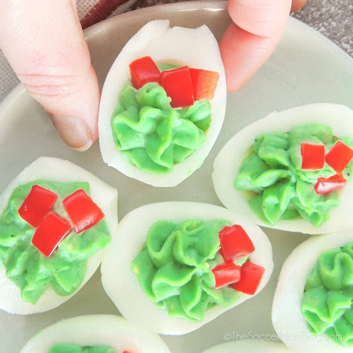 close up of a hand picking up a deviled egg that is red and green to look like a Christmas wreath.