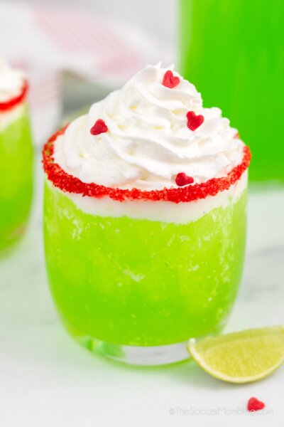 close up of a glass of bright green Grinch punch, topped with whipped cream and red heart sprinkles.
