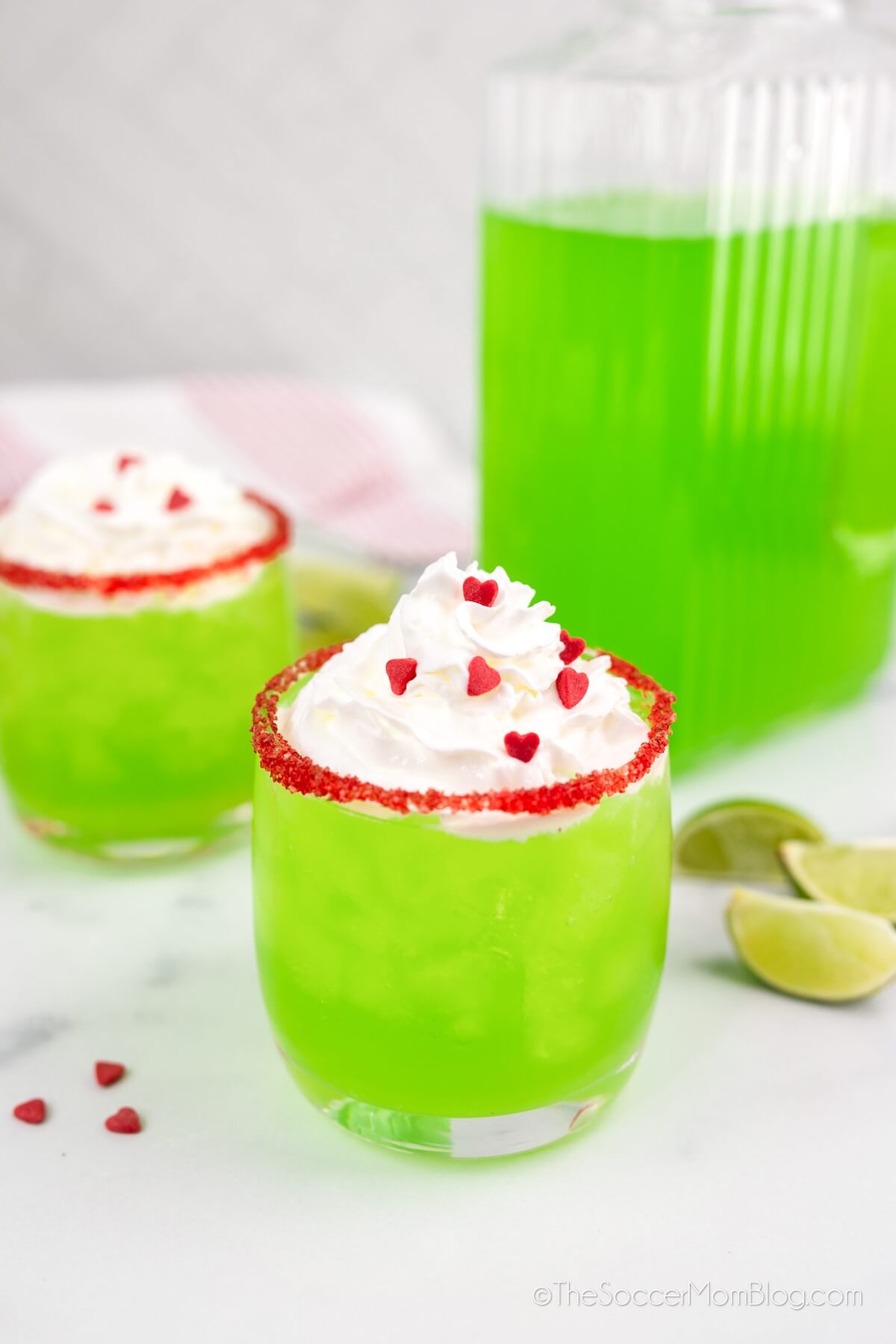 two glasses of lime green "Grinch Punch" with a drink pitcher in background.