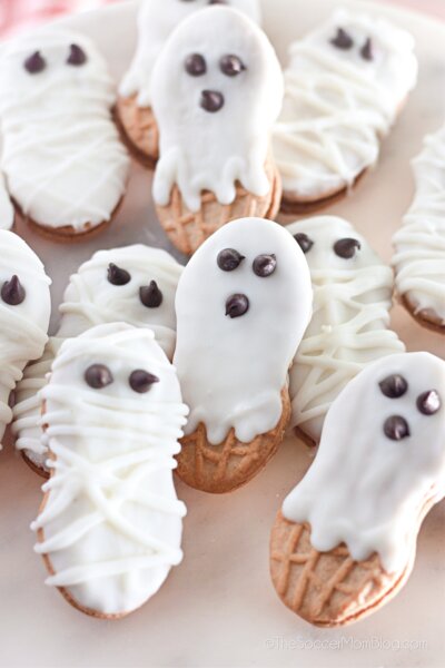 pile of Nutter Butter cookies that have been dipped in white chocolate and decorated to look like Halloween ghosts and mummies.