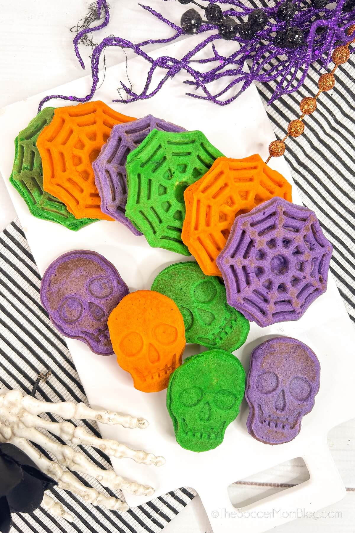 a plate of waffles shaped like skulls and spiderwebs, in orange, green and purple