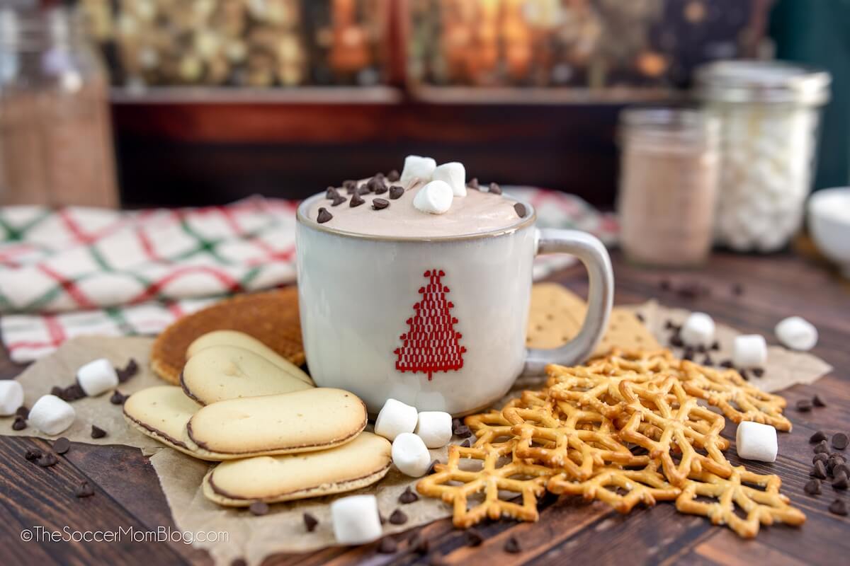 a mug of hot cocoa dip, surrounded by sweet treats like cookies and pretzels for dipping.