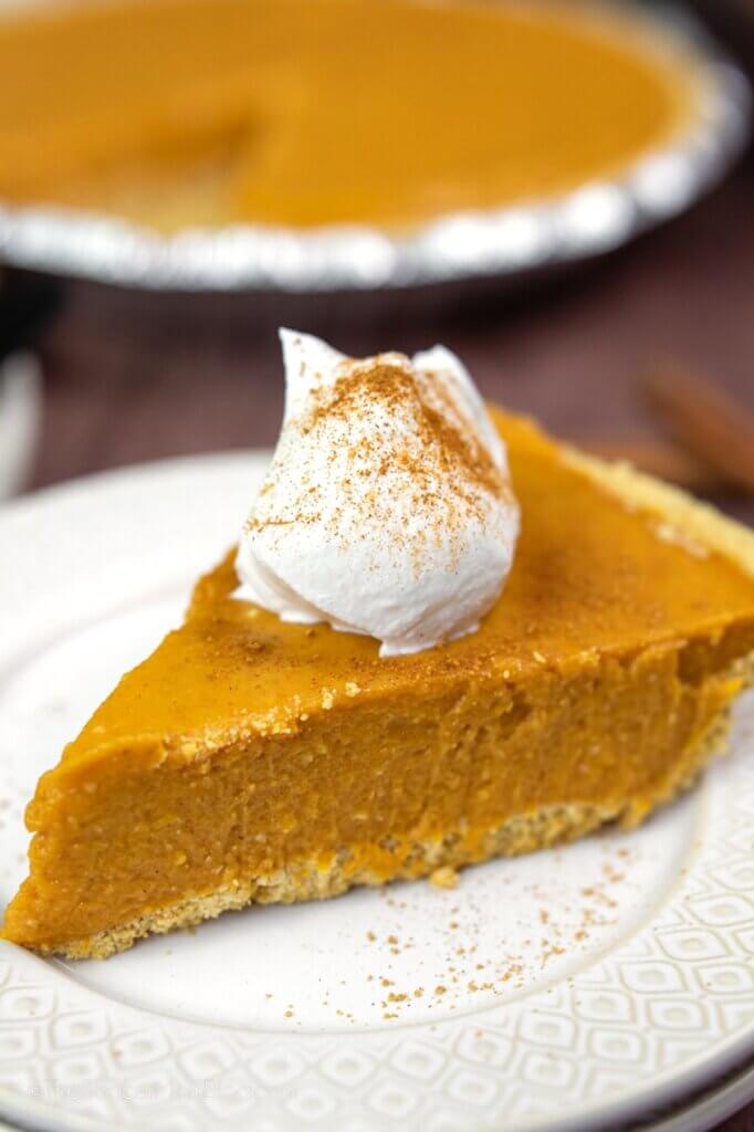 slice of homemade pumpkin pie with the full pie in background