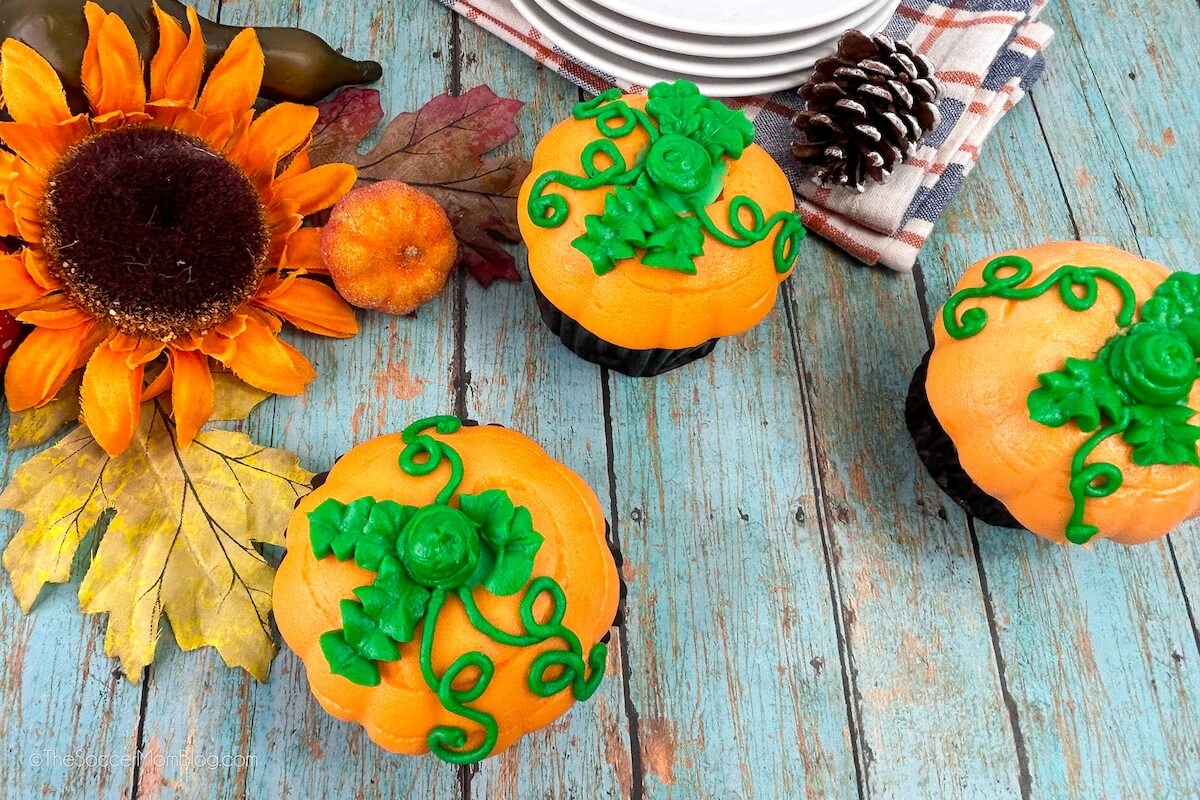 three pumpkin shaped cupcakes on a blue wooden surface.