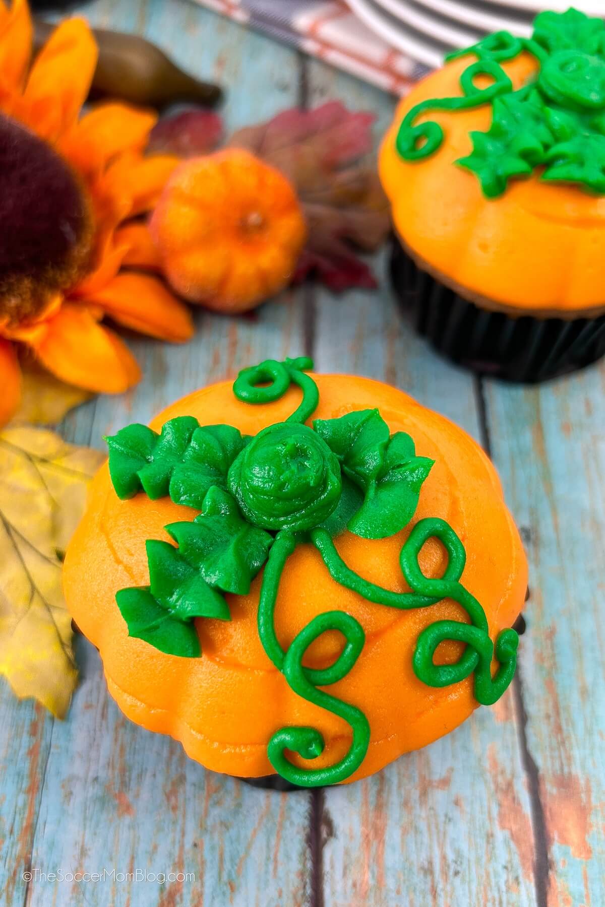 top down view of a cupcake with frosting on top that looks like an orange pumpkin with green leaves.