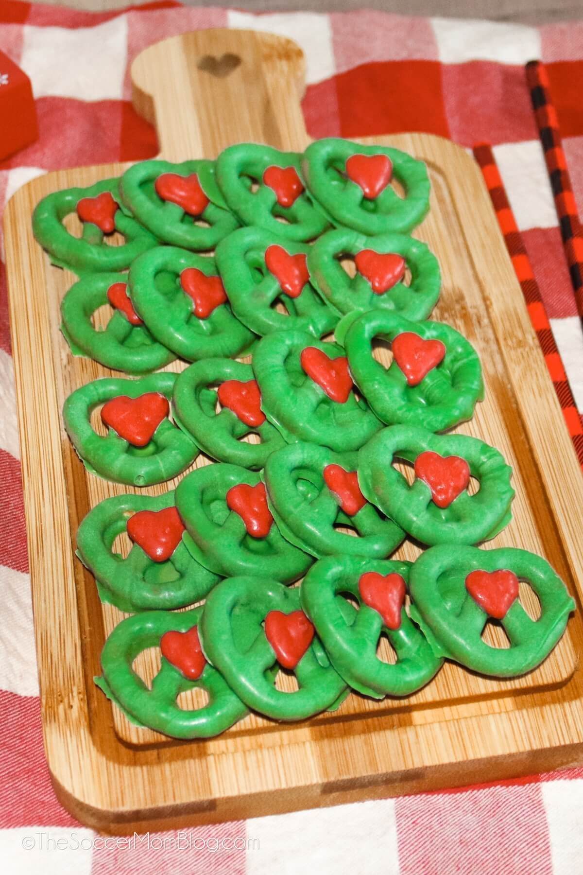 grinch pretzels dipped in green chocolate with a red chocolate heart in the middle.