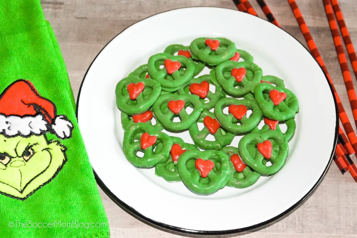 plate of green pretzels with a red heart in the center of each one, next to a towel with the Grinch face on it.
