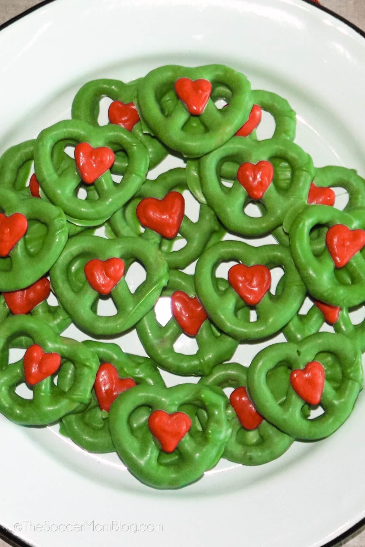 plate of green Grinch pretzels with a red candy heart on each one.