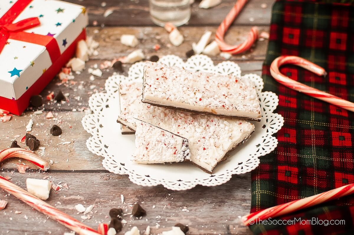 plate of peppermint bark squares, on a wooden surface with candy canes and a Christmas gift box.