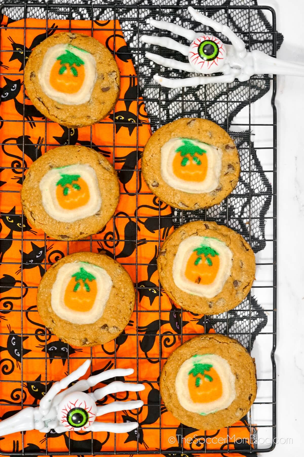 chocolate chip cookies topped with pumpkin shaped sugar cookies, on a wire rack.