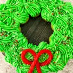 Christmas wreath made of cupcakes arranged in a circle with green frosting and a candy bow.