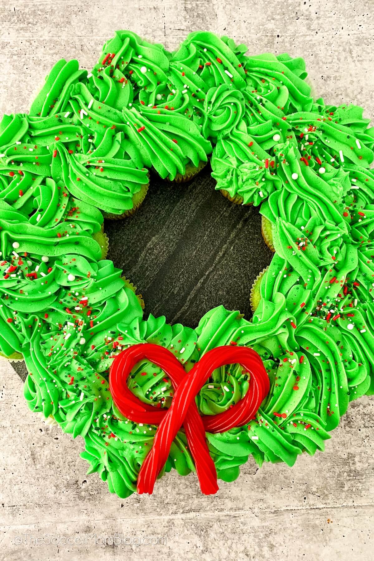 Christmas wreath made of cupcakes arranged in a circle with green frosting and a candy bow.