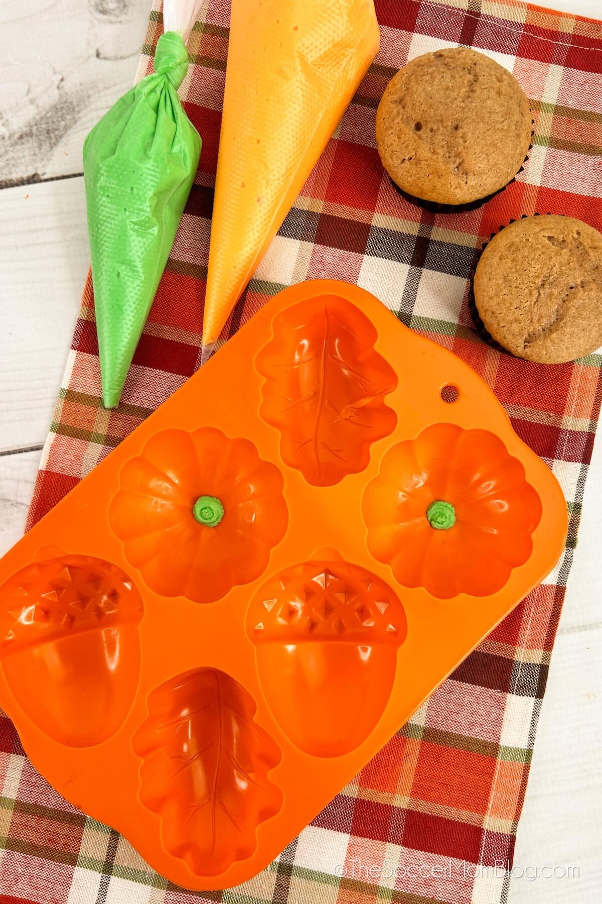 supplies to make pumpkin shaped cupcakes: orange and green frosting, pumpkin molds, and pumpkin cupcakes.