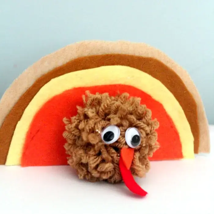 turkey craft made with a pom pom head and felt semi-circles as feathers.