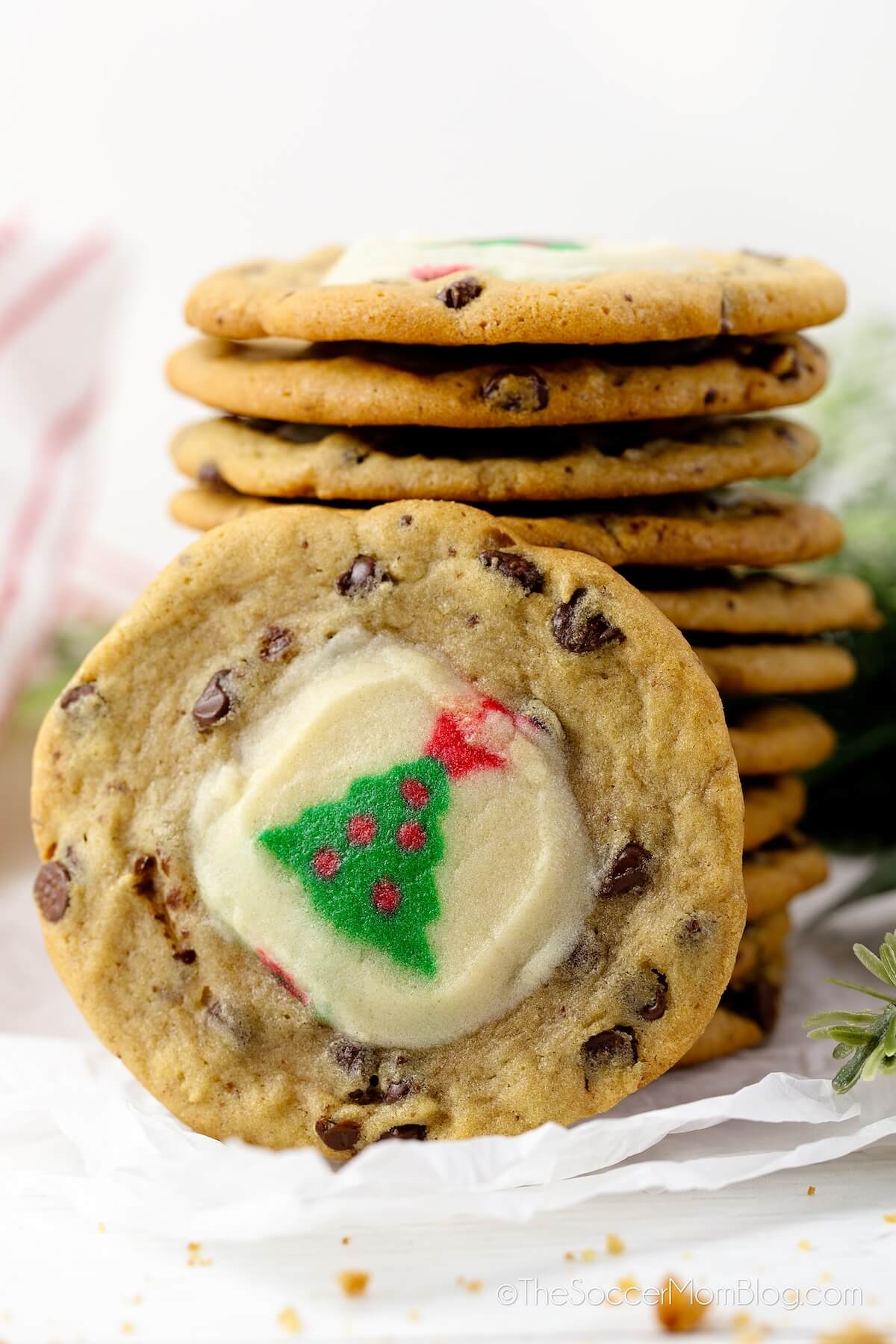chocolate chip cookie with a Christmas tree sugar cookie in the middle, with a stack of cookies in background.