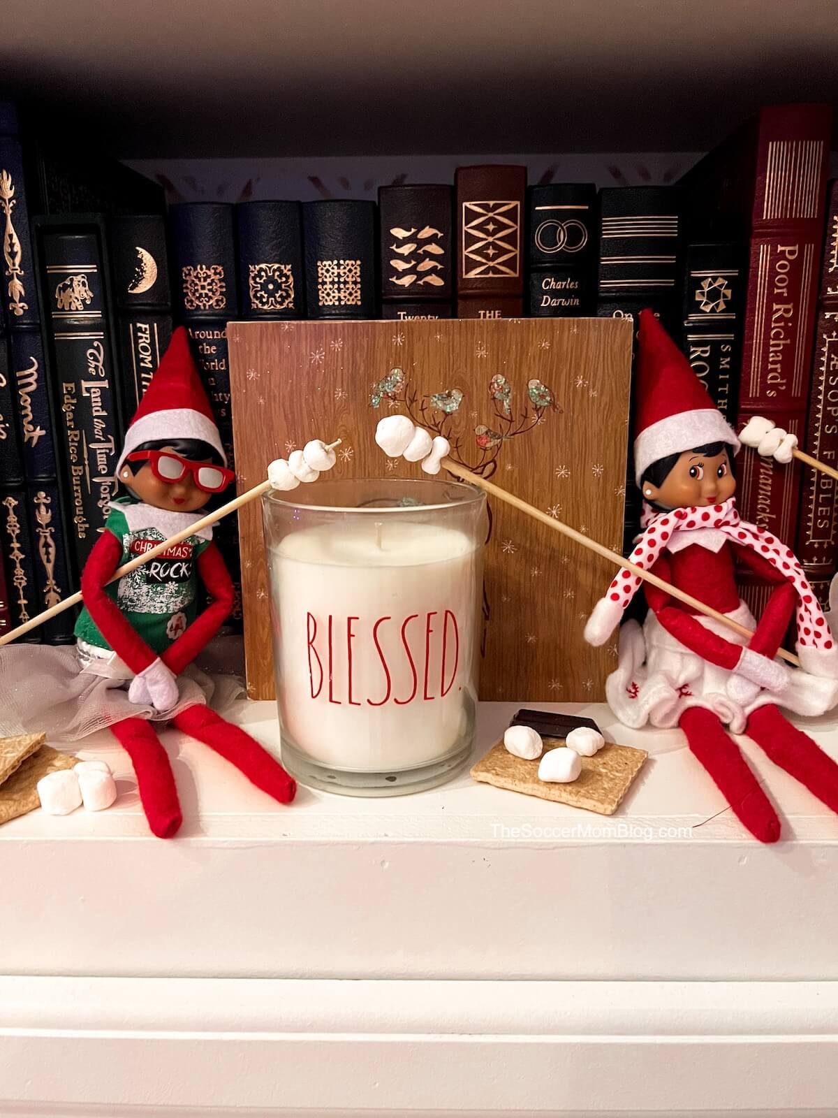 two Elf on the Shelf dolls pretending to roast marshmallows over a candle.