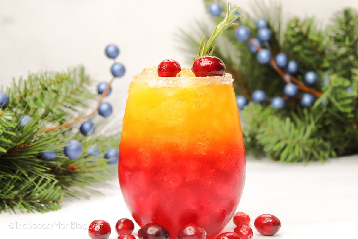 a red and gold layered holiday drink with pine decorations in background.
