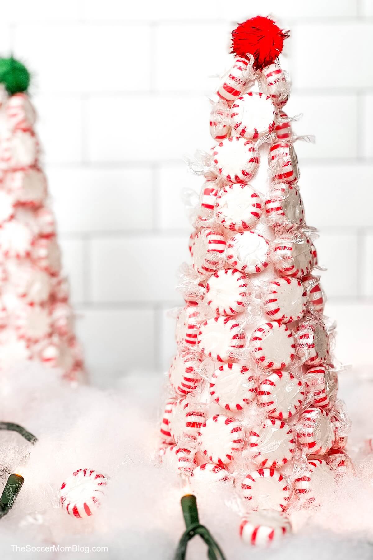 two Christmas trees made with peppermints, surrounded by decorative snow, lights, and mints.