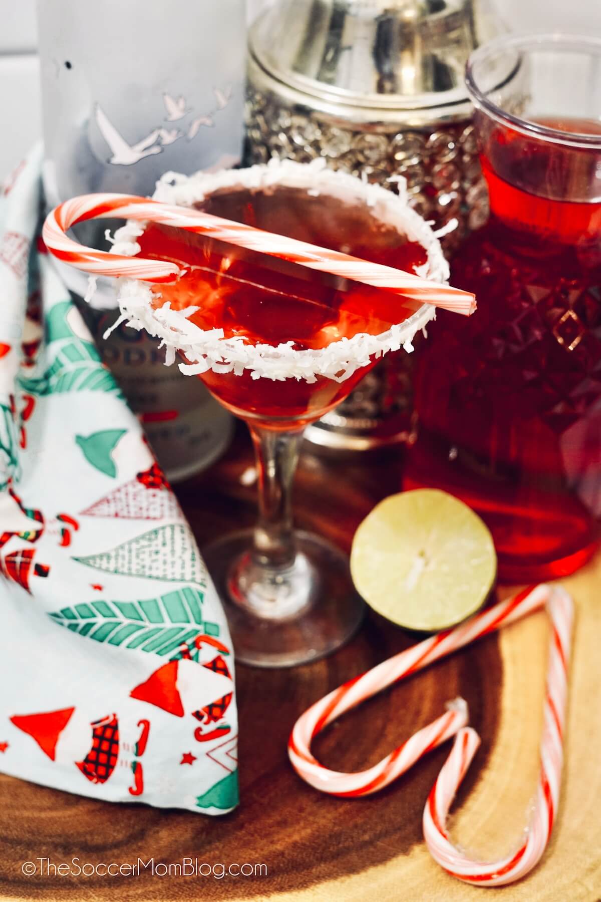 red martini with a coconut rim, surrounded by Christmas decorations and candy canes.