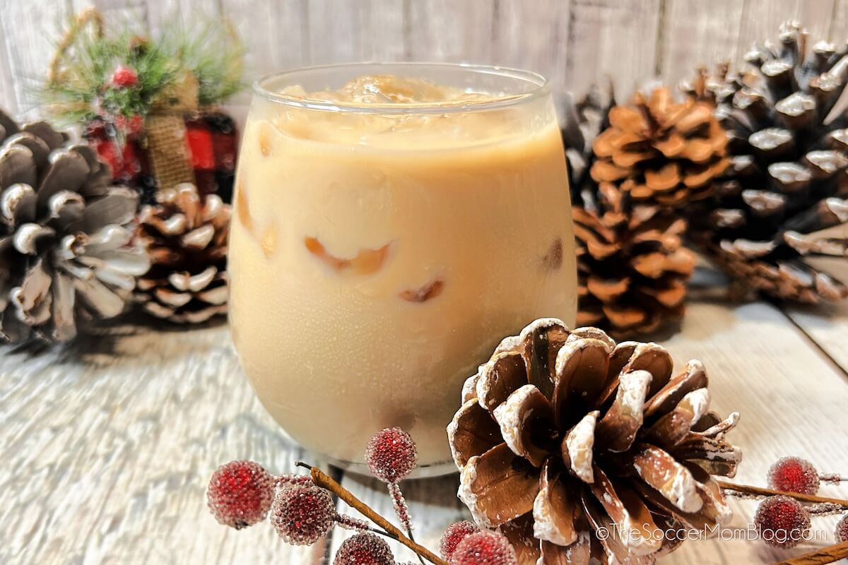 A creamy White Russian cocktail made with eggnog and surrounded by pinecone decor.
