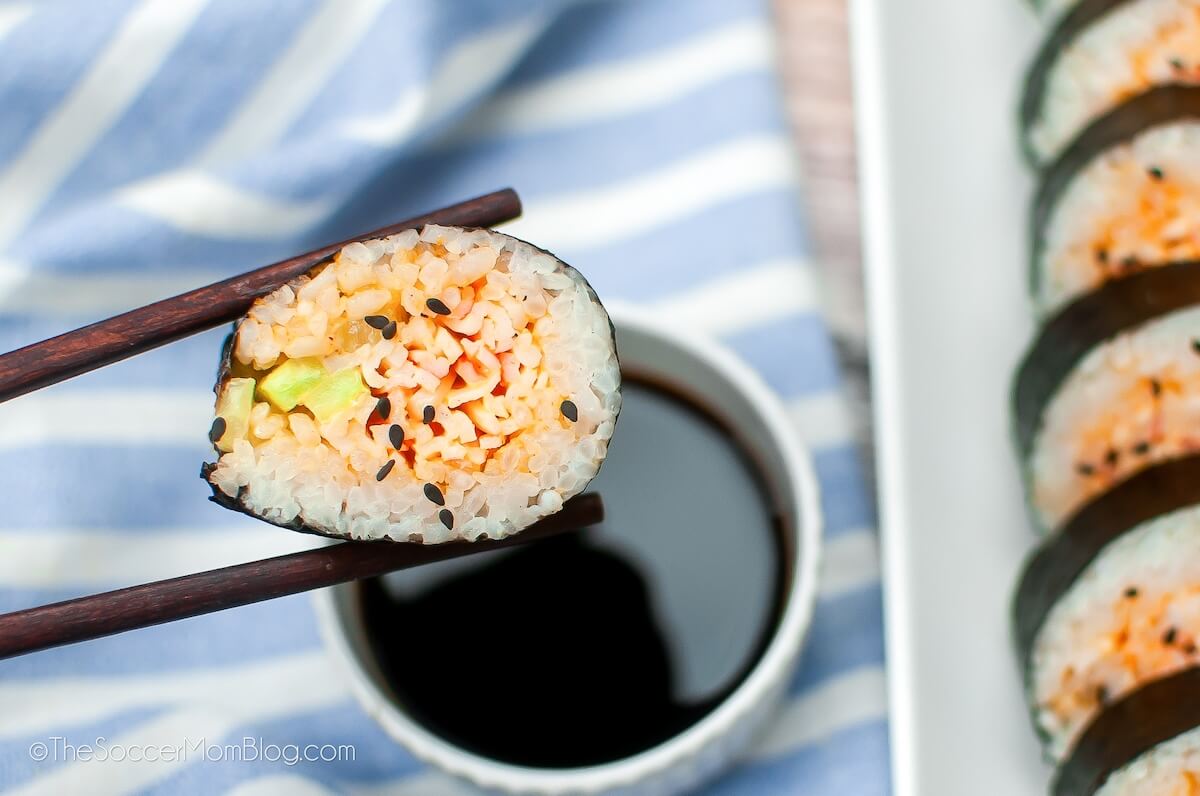 chopsticks holding a piece of Spicy Crab Sushi.