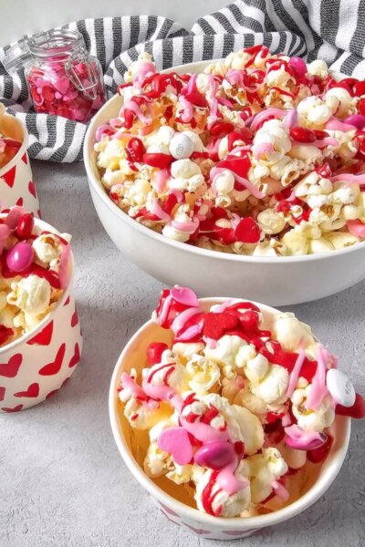 candy coated Valentine' Day Popcorn, in a large serving bowl and three small cups.