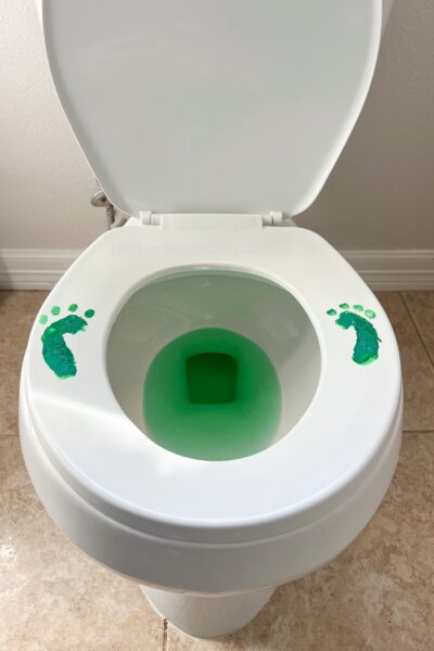 toilet with leprechaun footprints painted on seat and green water in bowl.