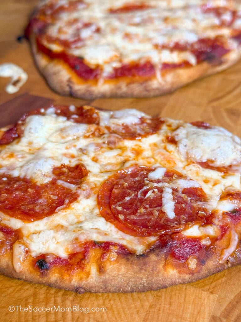close up of homemade naan pizza on a wooden cutting board.