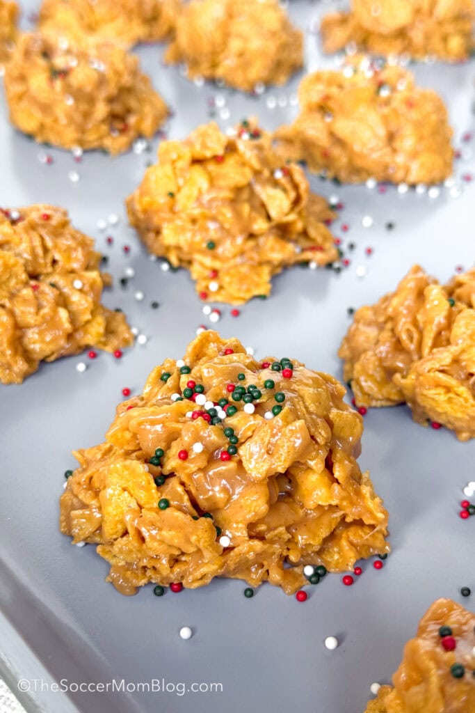 cornflake peanut butter clusters on a baking sheet topped with Christmas sprinkles.