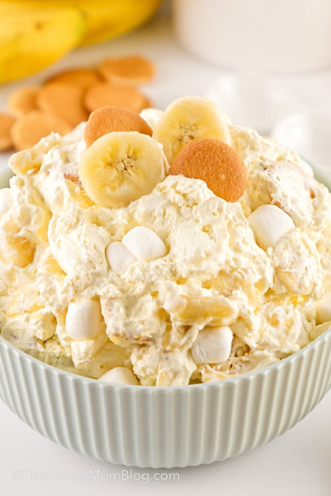 close up of a bowl of banana pudding fluff salad topped with mini marshmallows, vanilla wafers, and banana slices.