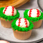 Three Baseball Cupcakes on a parchment line baking sheet.