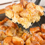 A slice of Donut Bread Pudding being lifted out of a pan on a spatula.