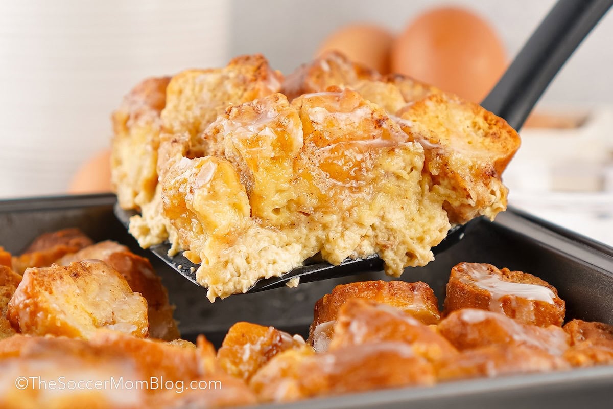 A slice of Doughnut Bread Pudding being lifted out of a pan.