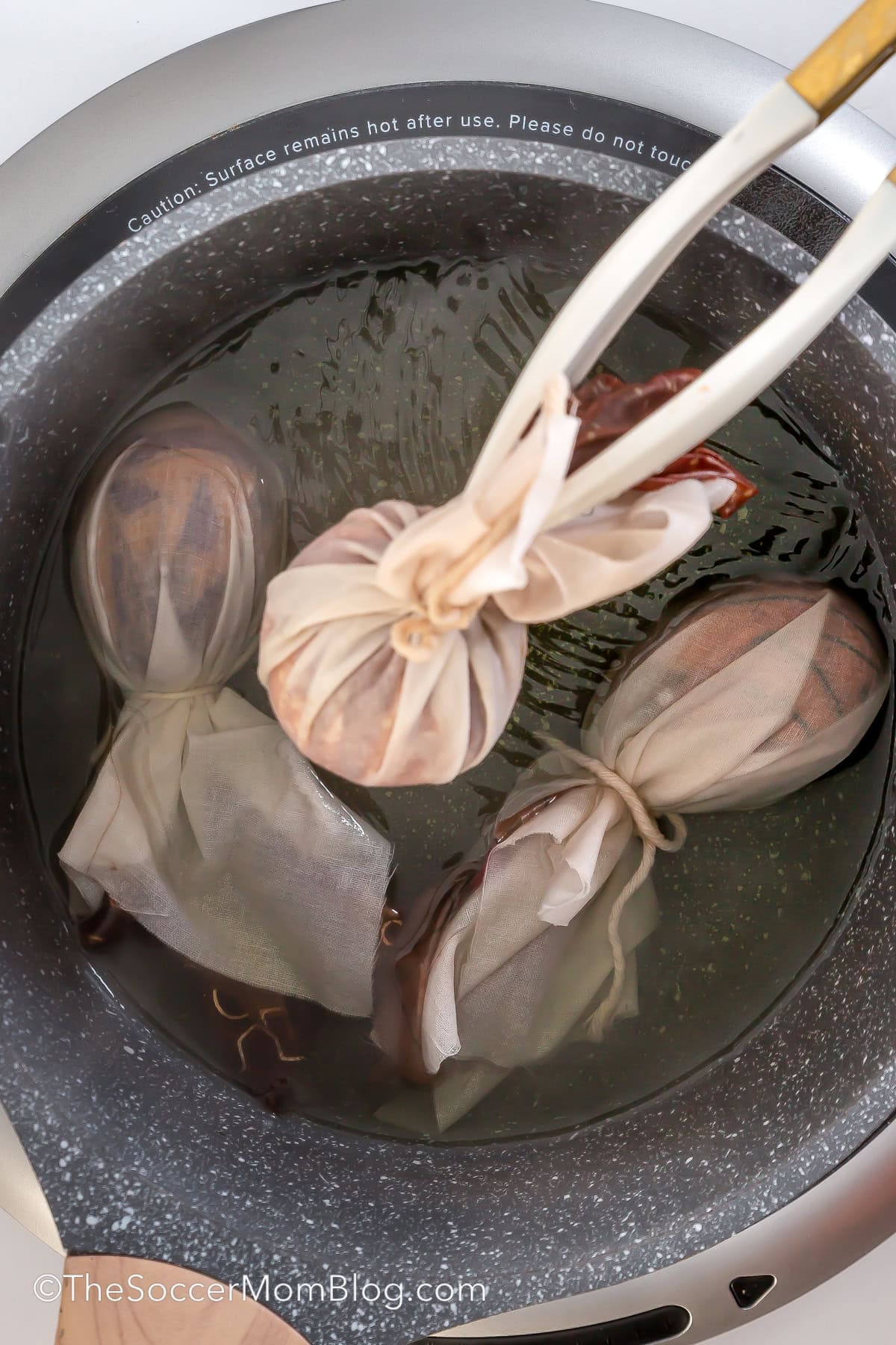 using tongs to remove silk-wrapped eggs from a pot of water.