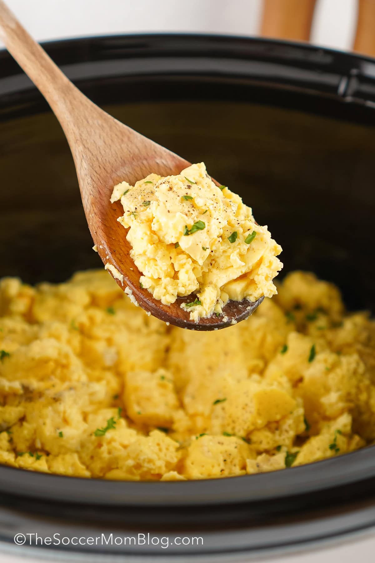 A wooden spoon with scrambled eggs on it.