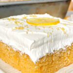 close up of a slice of lemon sheet cake topped with whipped cream.